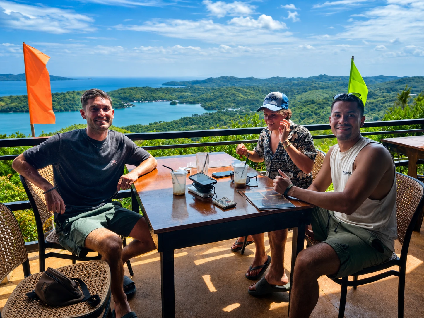 Three guests smiling at a table at Laaganan with a bright blue sea and island view behind them during the day.